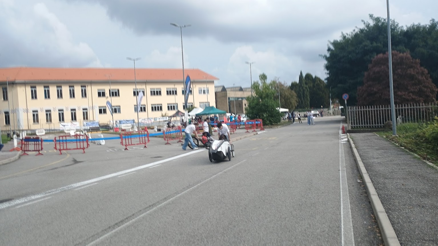 Un velomobile bianco percorre l’area della Festa dello Sport di Gozzano, con gli stand e le barriere sullo sfondo