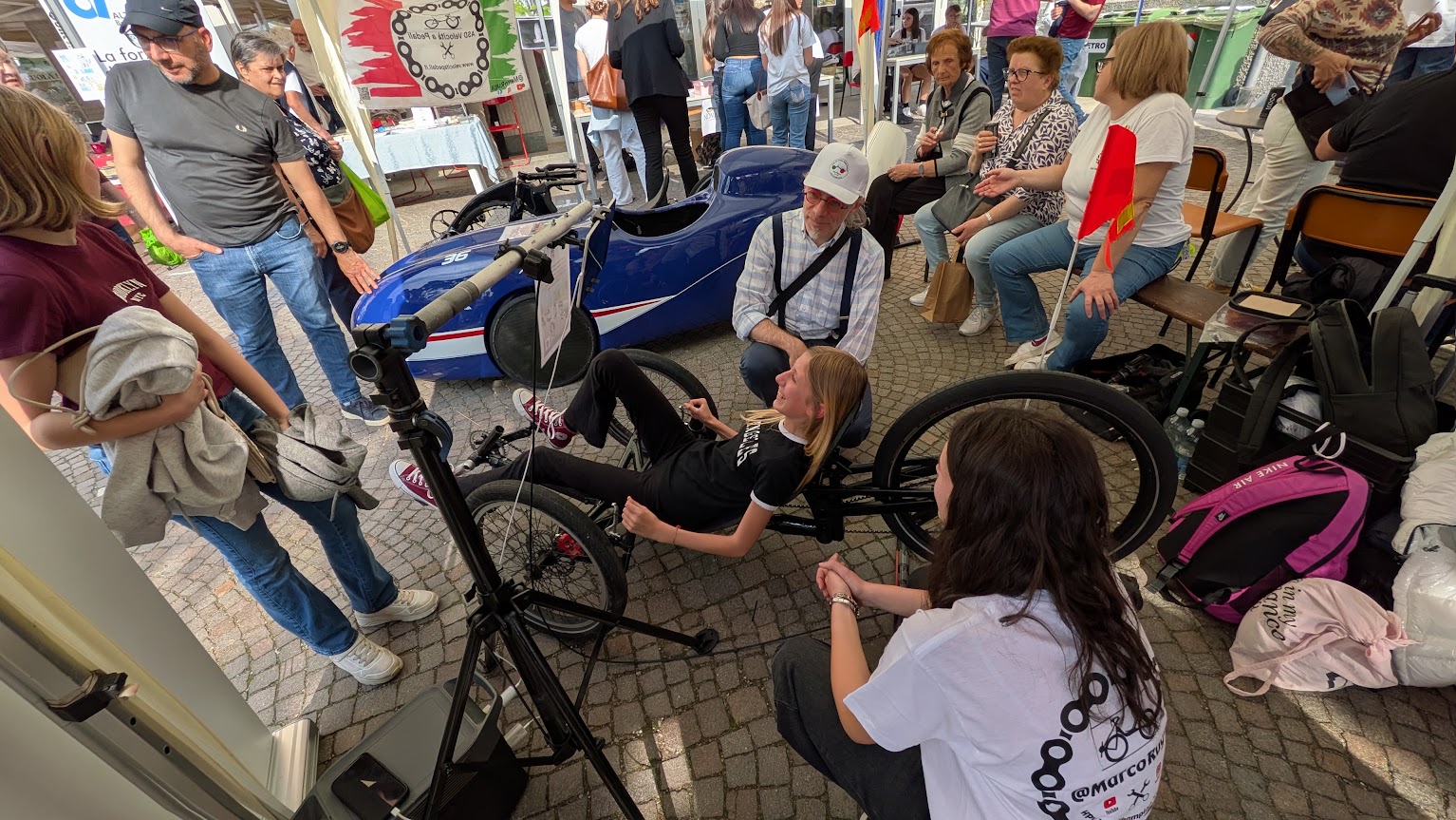 Visitatori osservano e provano una bicicletta reclinata allo stand ASD Velocità a Pedali