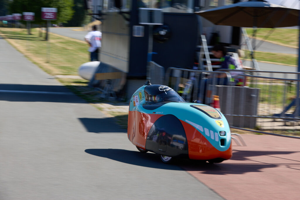 Un velomobile azzurro e arancione affronta il rettilineo del bike park durante la cronometro del Mondiale HPV 2026