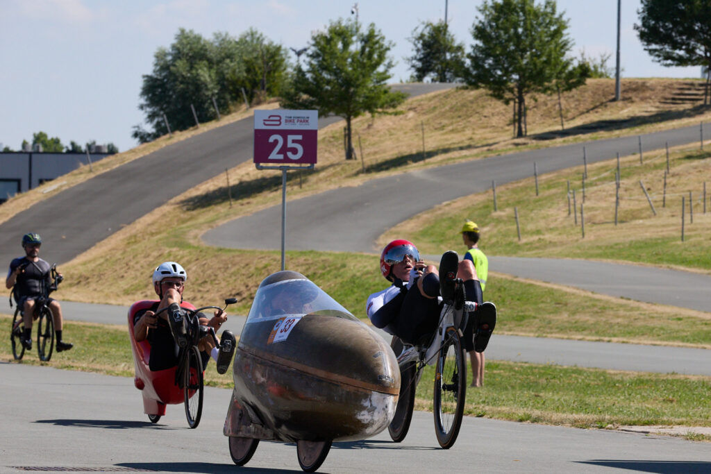 Un velomobile scuro guida un gruppo di biciclette reclinate e tricicli durante una gara a Sittard